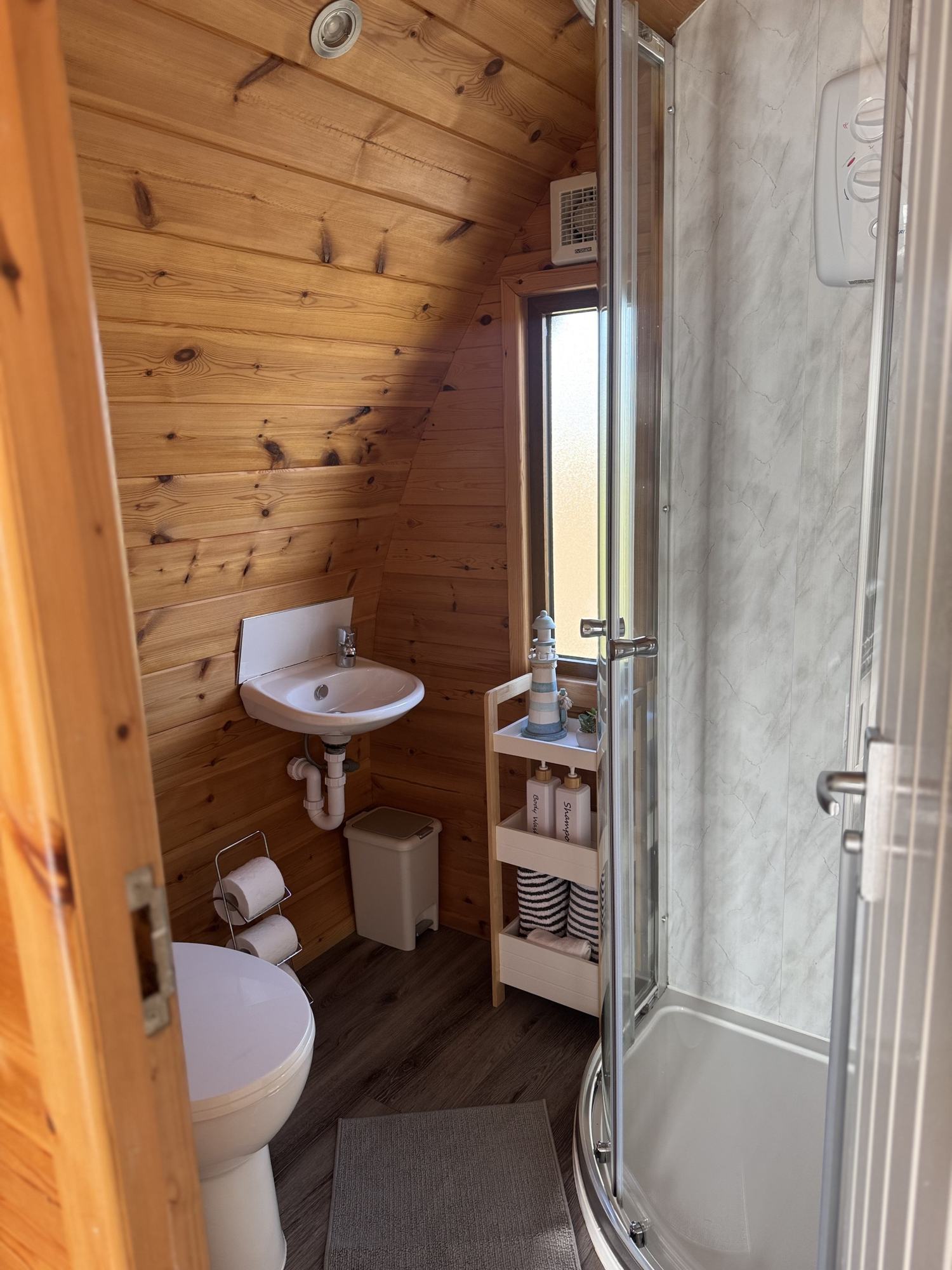 The en-suite shower room inside a pod, with pine-clad walls, a basin, WC and a corner shower.